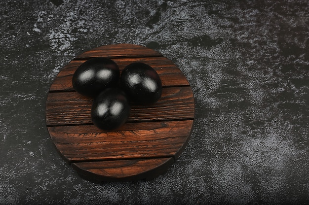 Ovos pretos em uma placa de madeira. configuração plana. Páscoa preta. três ovos pretos