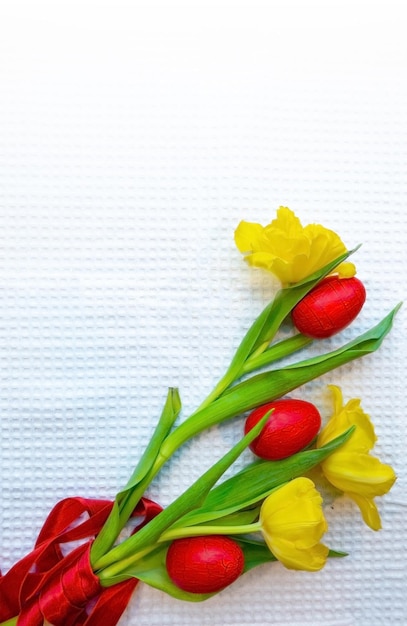 Foto ovos vermelhos estão deitados na mesa entre tulipas amarelas amarradas com uma fita escarlate um prato com ovos de codorniz ninhos de caviar e uma estatueta de frango feita de gemas é o conceito de um prato de páscoa