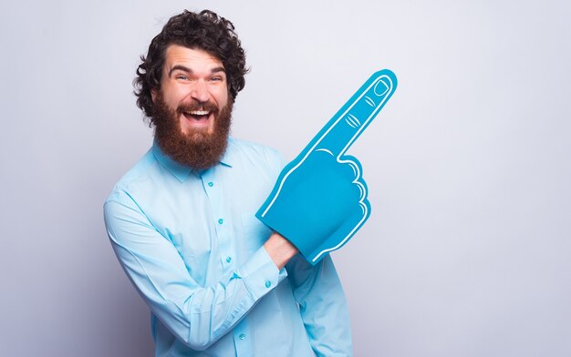 Oye, mira esto, hombre alegre apuntando hacia afuera con un guante de espuma azul