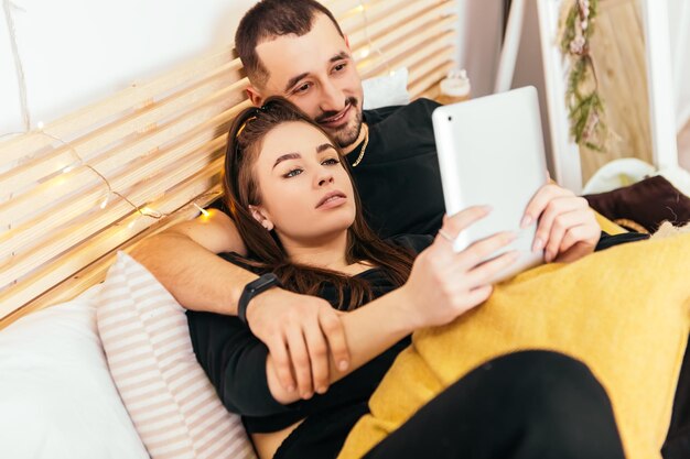 Paar auf dem Bett liegend in Decke gewickelt und Tablet halten