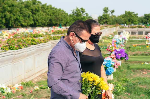 Paar auf Trauerfriedhof mit gelben Blumen in den Händen