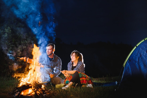 Paar Backen von Würstchen am Feuer und Entspannen am Lagerfeuer im Wald in der Nacht