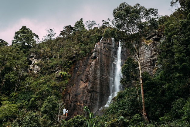 Paar bewundert einen schönen Wasserfall. Verliebtes Paar am Wasserfall. Jungen und Mädchen an den Wasserfällen. Ein Mann und ein Mädchen reisen. Das Paar reist durch Asien. Wasserfälle in Sri Lanka. Flitterwochen