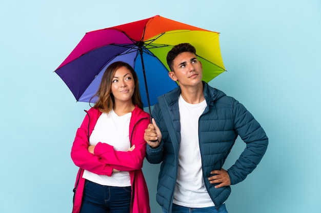 Paar, das einen Regenschirm auf Blau hält und beim Lächeln nach oben schaut