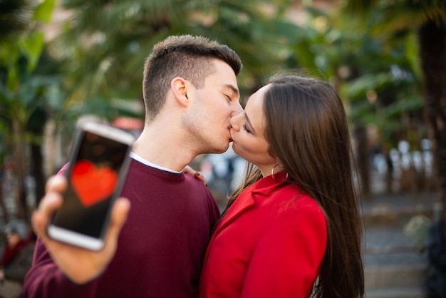 Paar, das küsst, während ein Smartphone mit einer Herzform darin zeigt, Datierungsanwendungskonzept