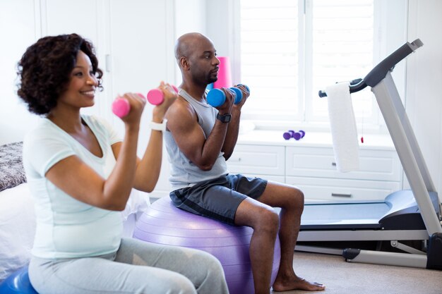 Paar, das mit Hanteln auf Fitnessball im Schlafzimmer trainiert