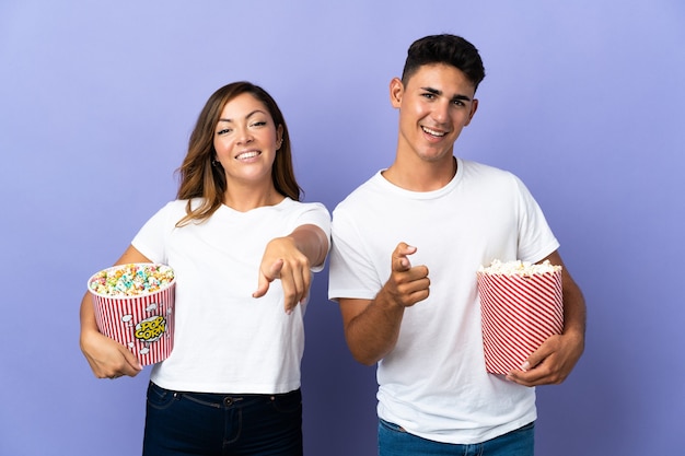 Paar, das Popcorn isst, während Sie einen Film auf lila Zeigefinger mit einem selbstbewussten Ausdruck auf Sie sehen