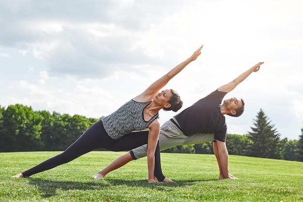 Paar dehnt sich junges Paar aus und macht Yoga-Übungen in der Natur an einem sonnigen Morgen