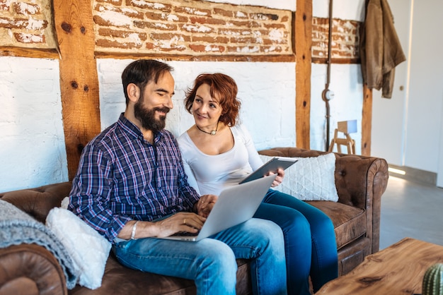 Paar entspannt zu Hause auf der Couch auf dem Computer und Tablet