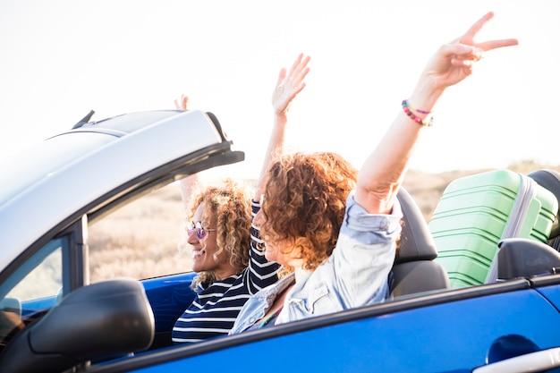 Paar erwachsene kaukasische Frauen in einem Cabrio und Gepäck hinter den Sitzen