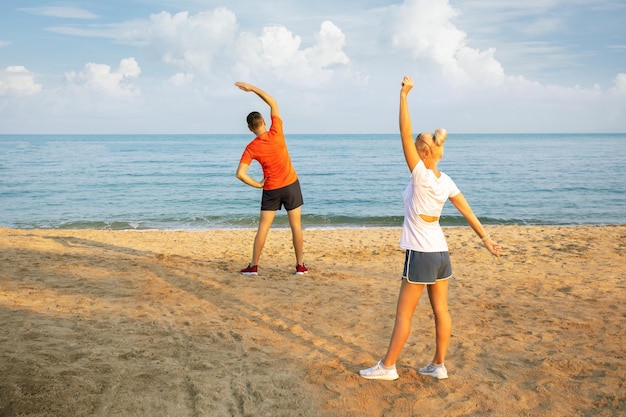 Paar Familie starke sportliche Sportlerin Sportler Frau Mann in Sportkleidung Aufwärmtraining tun Dehnungsübungen am Sand Meer Ozean Strand im Freien