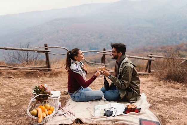 Paar feiert Jubiläum auf Picknick. Paar sitzt auf Decke und jubelt mit Wein. Herbstzeit.