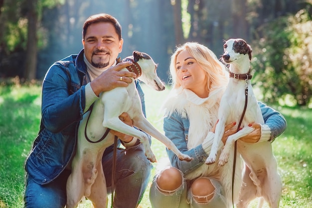 Paar Frau und Mann in Denim-Kleidung, die mit Whippets Hunden im Freien spazieren geht