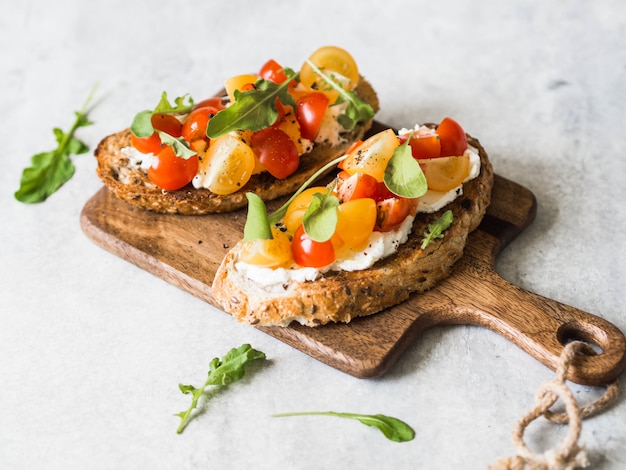 Foto paar gegrillte toasts mit frischkäse und scheiben von frischen tomaten in verschiedenen farben mit frischem rucola und gemahlenem schwarzem pfeffer