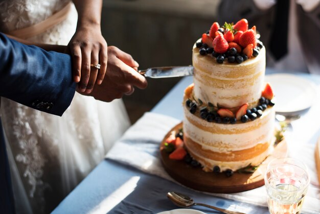 Paar-Hände, die Hochzeitstorte schneiden