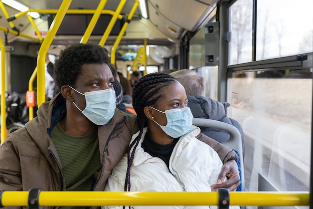 Paar im bus, der masken trägt, während er in neuen normalen afrikanischen männern und frauen in öffentlichen verkehrsmitteln reist