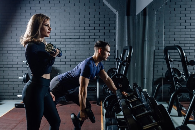 Paar im Fitnessstudio mit Hanteln, die Gewicht als Sport-, Mann- und Frauentraining zusammen heben