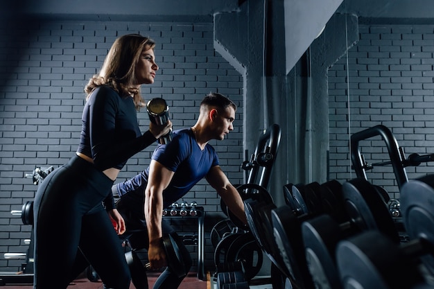 Paar im Fitnessstudio mit Hanteln, die Gewicht als Sport-, Mann- und Frauentraining zusammen heben