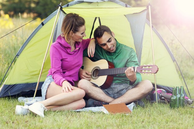 Paar im Wald campen und Gitarre spielen