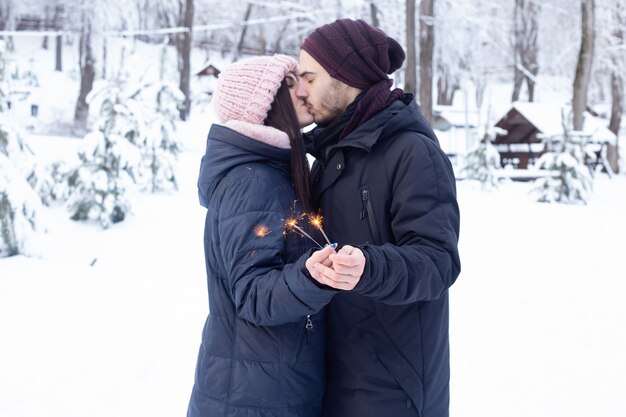 Paar in Liebe küssen, während das Halten funkelt im Park mit Schnee