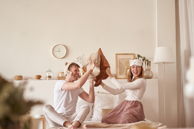 Paar in Liebe lachen und spielen auf dem Bett. Mann und Frau kämpfen Kissen. Junges glückliches Paar schlug die Kissen auf dem Bett in einem Schlafzimmer zu Hause