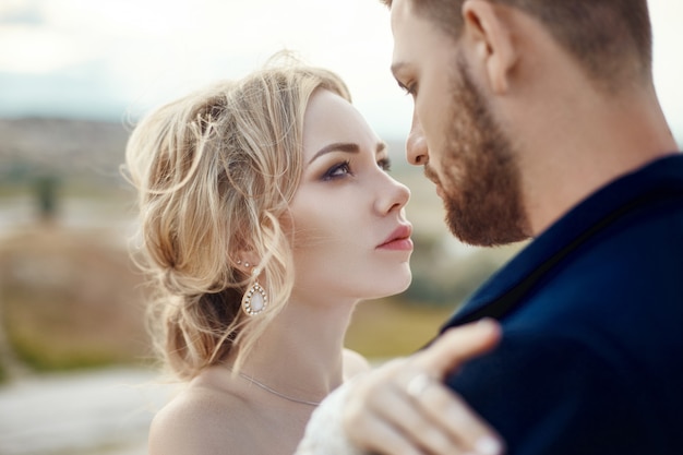 Paar in Liebe Umarmungen und Küsse in fabelhaften Bergen in der Natur. Mädchen im langen weißen Kleid mit Blumenstrauß in ihren Händen, Mann in der Jacke. Hochzeit in der Natur, Beziehungen und Liebe