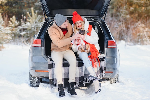 Paar Kerl und Mädchen sitzen im Auto und spielen mit Hund im Winterwald