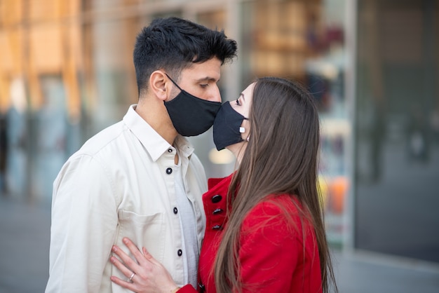 Paar küssen beim Tragen einer Covid- oder Coronavirus-Maske, pandemisches Liebeskonzept