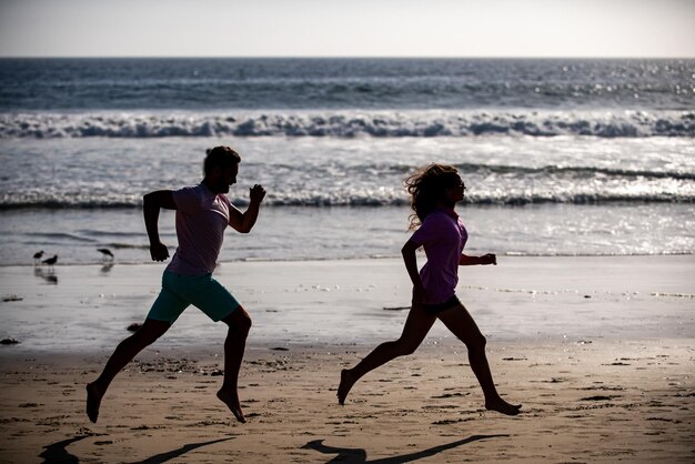 Paar läuft am Strand. Sport und gesunder Lebensstil, Silhouettenfreunde, die bei Sonnenuntergang am Strand joggen.