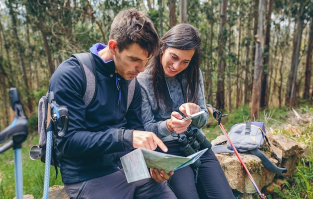 Paar macht Trekking sitzend und schaut auf Handy und Karte