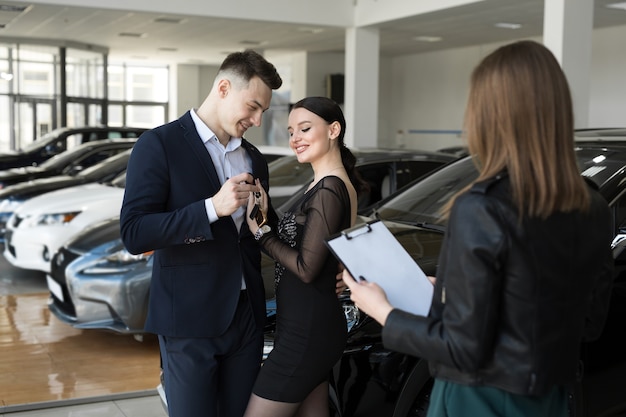 Paar Mann und Frau kaufen gerne ein neues Auto in einem Autohaus mit dem Verkäufer