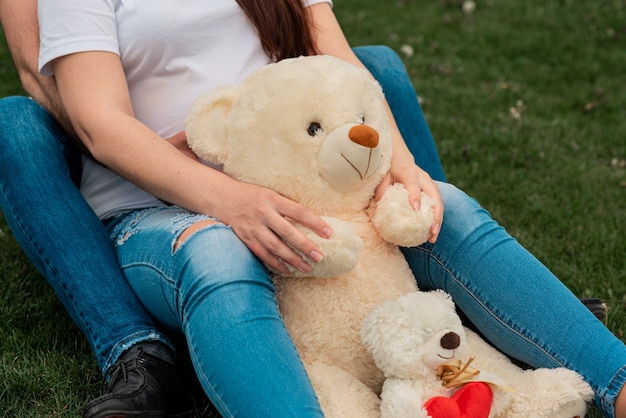 Paar mit der schwangeren Frau, die auf Gras mit Spielzeugbär liegt