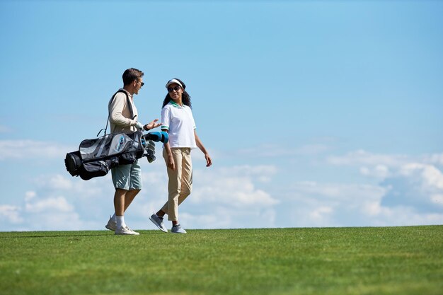 Paar mit Golftasche zu Fuß auf der grünen Wiese vor blauem Himmel