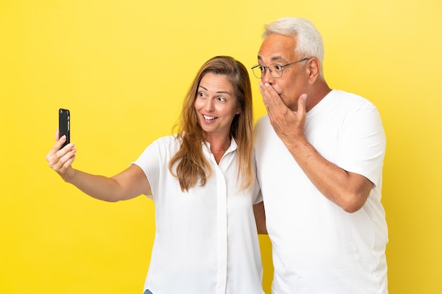 Paar mittleren Alters isoliert auf gelbem Hintergrund, der ein Selfie mit dem Handy macht