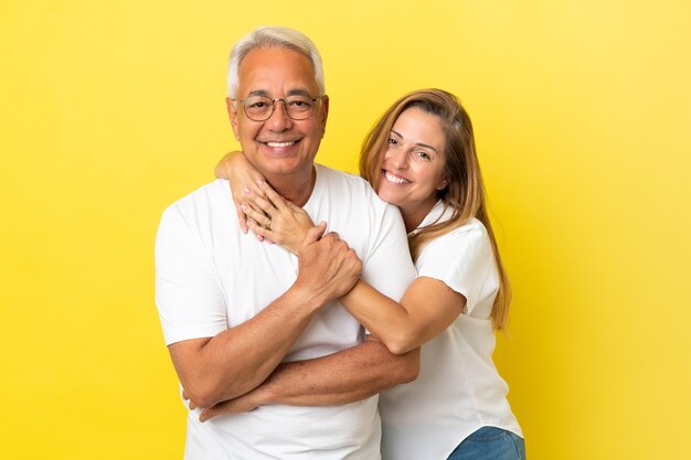 Paar mittleren Alters isoliert auf gelbem Hintergrund lachen und umarmen