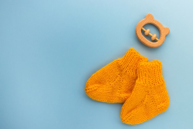 Paar niedliche orange gestrickte Babysocken und hölzerner Beißringbär auf Blau