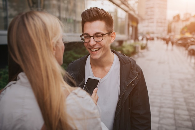 Paar oder freunde, die lustig lachen und spaß mit einem smartphone in einer großstadtstraße haben.