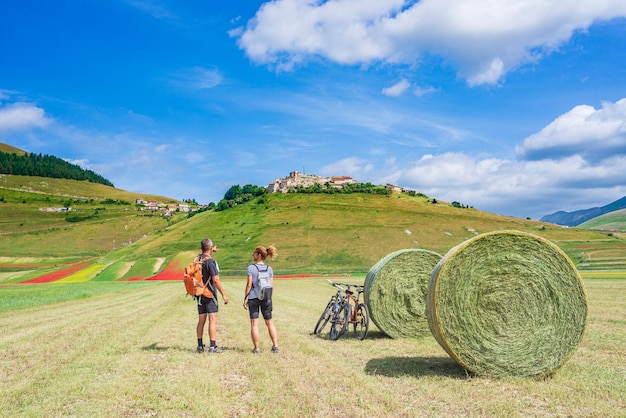 Paar Radfahren mtb in blühenden Feldern des Hochlandes von Castelluccio di Norcia berühmte bunte blühende Ebene in den Apenninen Italien Landwirtschaft von Feldfrüchten und roten Mohnblumen