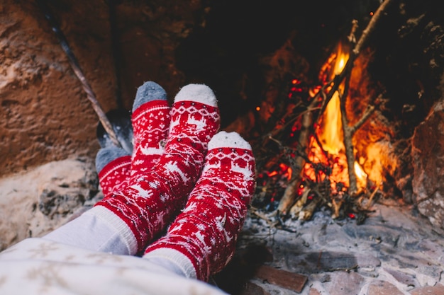 Paar rote, weihnachtlich dekorierte Socken, die in der Weihnachtsferienzeit vor einem Kamin mit Wods heizen. Konzept von Menschen, die mit Romantik und Liebe feiern. Mann und Frau genießen Chalet