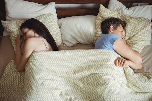 Paar schläft Rücken an Rücken und ignoriert sich gegenseitig auf dem Bett