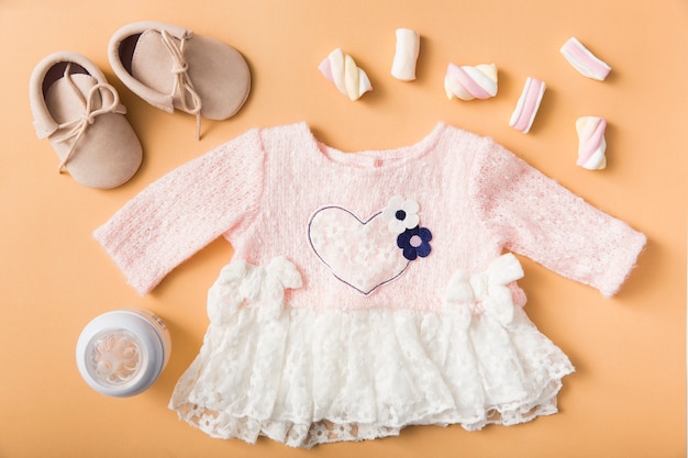 Paar schuhe; marshmallow; milchflasche und baby rosa kleid auf einem orangefarbenen hintergrund