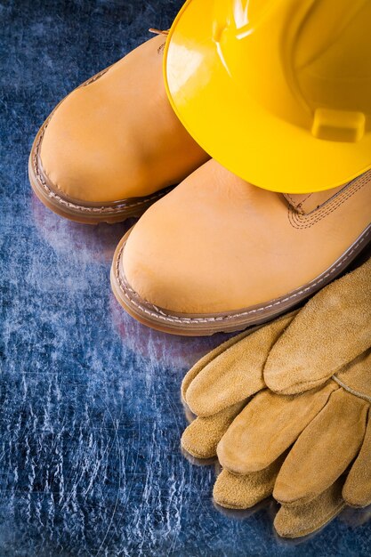 Paar Sicherheitsstiefel Handschuhe und Arbeitshelm auf zerkratztem metallischem Oberflächenkonstruktionskonzept