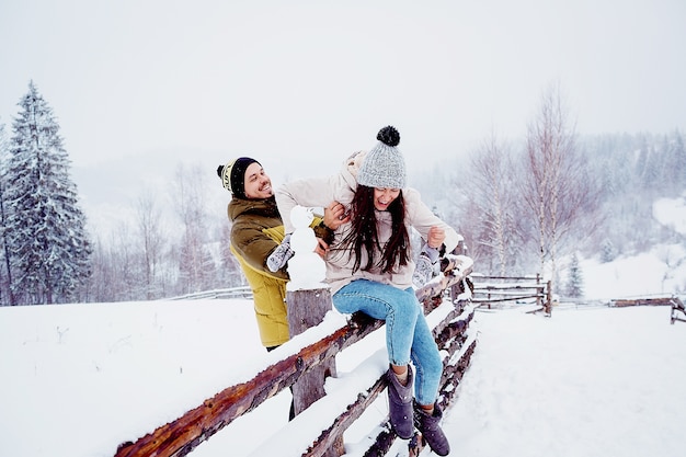 Paar sieht lustig auf dem Zaun mit Schneemann sitzen
