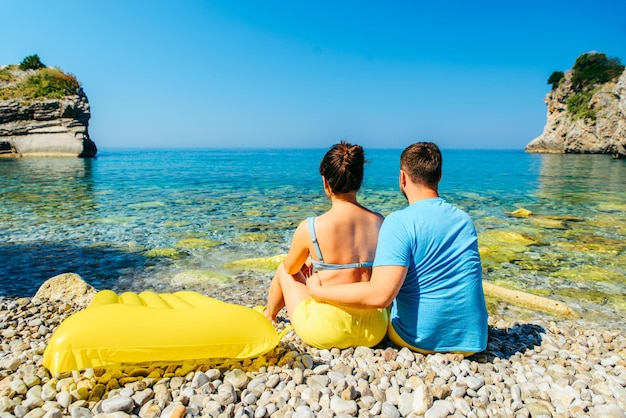 Paar sitzt am felsigen Strand und blickt aufs Meer