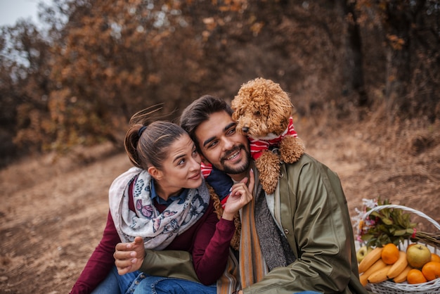 Foto paar sitzt am picknick und spielt mit hund.