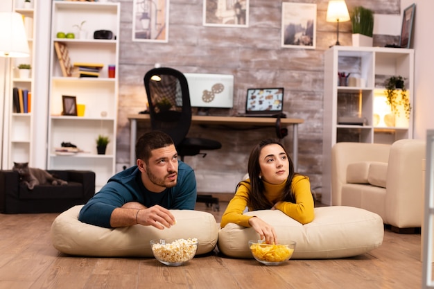 Paar sitzt auf dem Boden und sieht im Wohnzimmer fern.