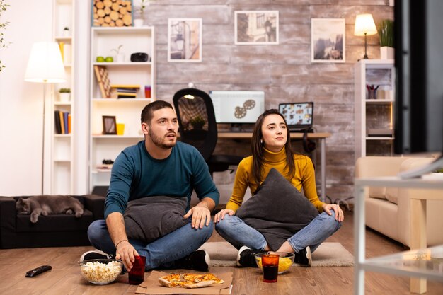 Paar sitzt auf dem Boden und sieht im Wohnzimmer fern.