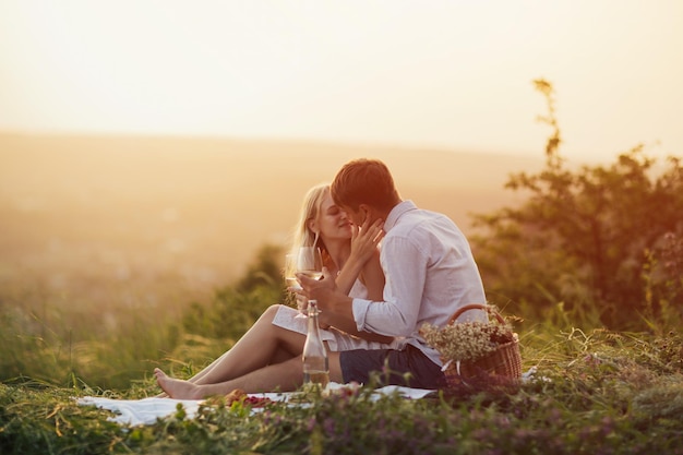 Paar sitzt auf dem Hügel und trinkt Weißwein bei Sonnenuntergang