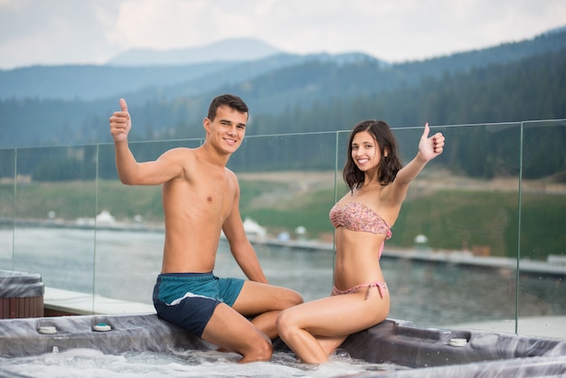 Paar sitzt auf dem Jacuzzi gesenkte Füße im Wasser und zeigt Daumen hoch Geste der guten Klasse