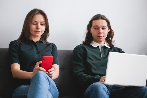 Paar sitzt auf dem Sofa mit Notebook und Telefon Mann und Frau kommunizieren auf dem Laptop-Telefon